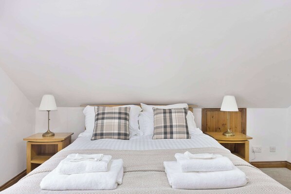 A neatly made bed with plaid pillows, two bedside lamps, and folded towels on a wooden nightstand. - The Roost Group - 8-Bed Home: Hot Tub WiFi Parking (Gravesend)