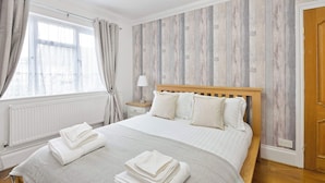 Una cama bien hecha con almohadas, una mesita de noche con lámpara y una ventana con cortinas.