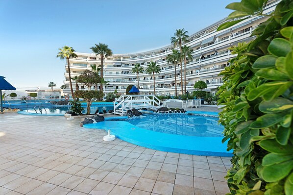 A hotel with a pool area, palm trees, and a multi-story building.