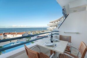 Un balcon avec une table dressée pour le dîner, donnant sur une piscine et un port de plaisance.