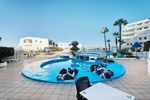 Une piscine avec des rochers, un bâtiment blanc et des palmiers.