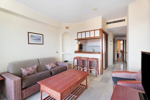A living room with a sofa, a wooden table, and a kitchen area with stools.