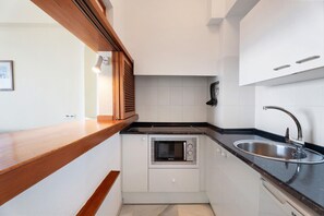 A compact kitchen with a built-in microwave, a sink, and wooden cabinetry.