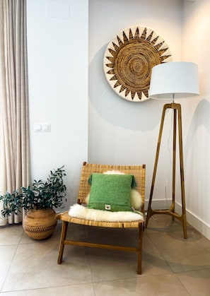 A wicker chair with a green pillow, a round woven wall decoration, a floor lamp, and a potted plant.