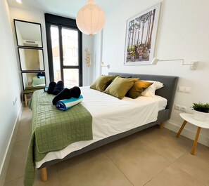 A bedroom with a bed, a bedside table with a plant, a mirror, and a window.