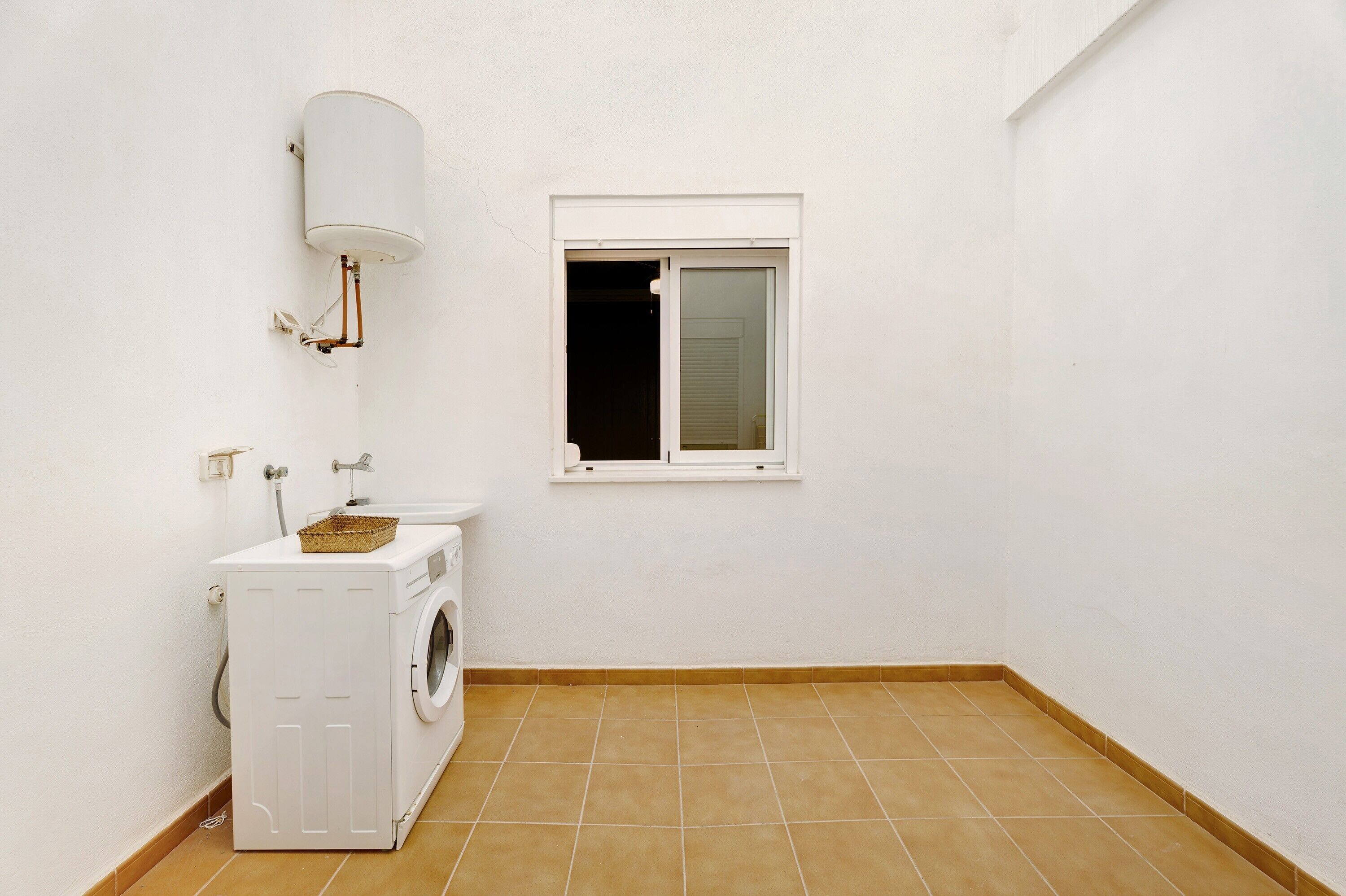 A small, clean laundry room with a washing machine, a utility sink, and a window.
