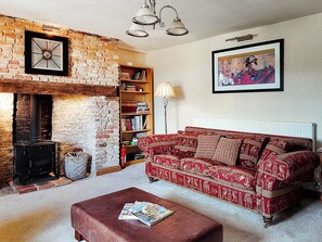 A cozy living room with a fireplace, a red patterned sofa, a bookshelf, and a framed picture on the wall. - 5 bedroom accommodation in Pentney, King&rsquo;s Lynn (Pentney, King&rsquo;s Lynn)