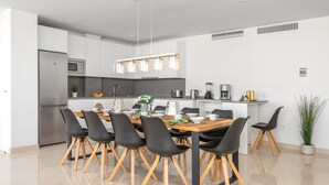 Une cuisine moderne dotée d’un îlot central, d’appareils électroménagers en acier inoxydable et d’un coin repas avec des chaises noires et une table en bois.