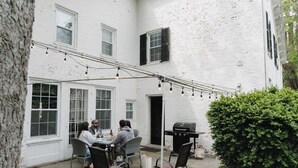 A white brick building with a patio area featuring outdoor seating and a grill. - Historic Home: Game Room & Fire Pit, Near Downtown (Geneva)
