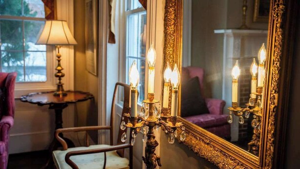 A room with a large ornate mirror, a candelabra with lit candles, a chair, and a table with a lamp. - Historic Home: Game Room & Fire Pit, Near Downtown (Geneva)