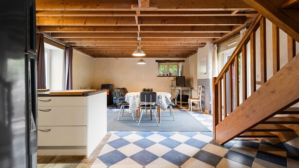 Une pièce spacieuse avec un sol à carreaux, une table à manger avec des chaises, un coin cuisine et un escalier.