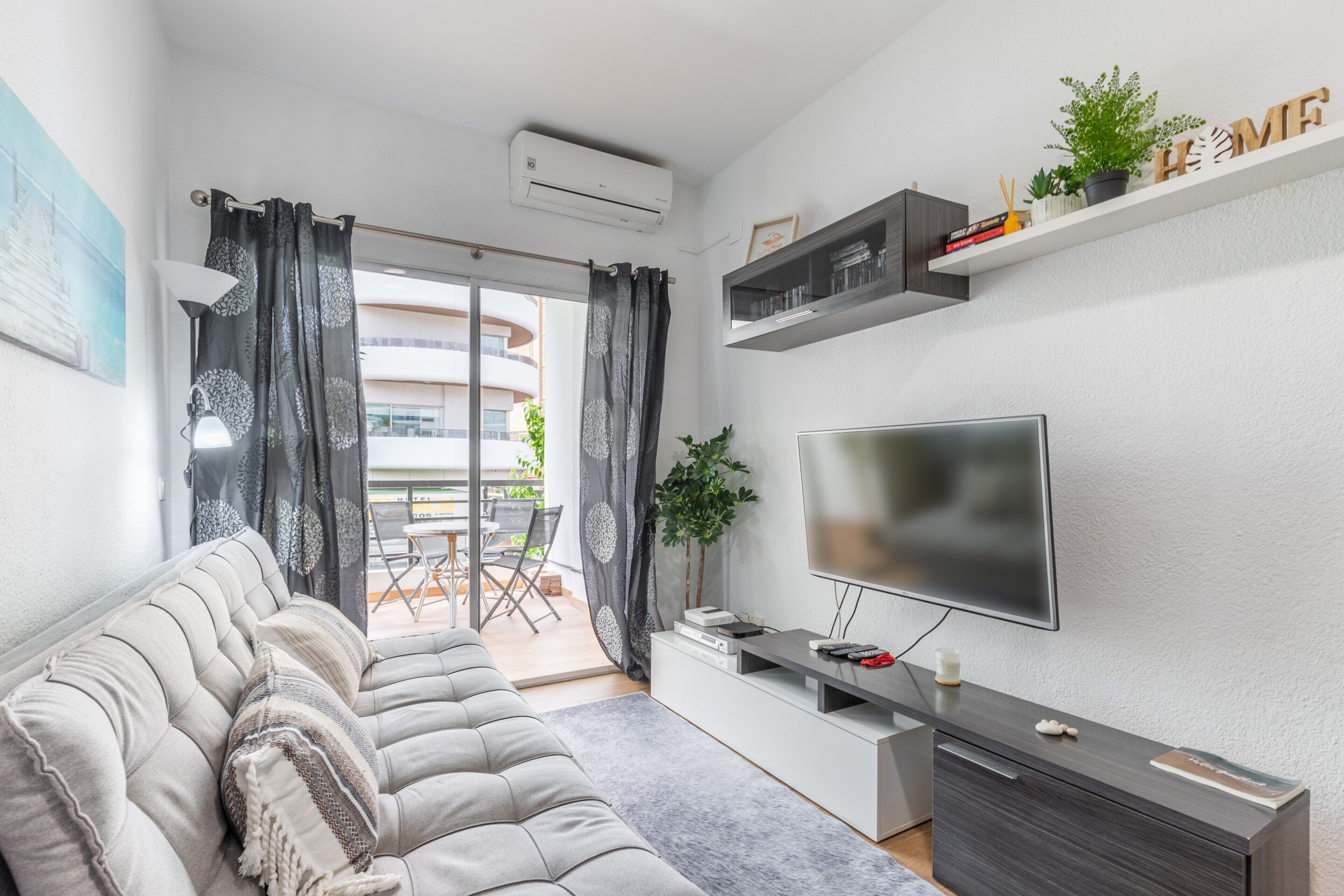 A modern living room with a sofa, TV, and a balcony with a dining area.