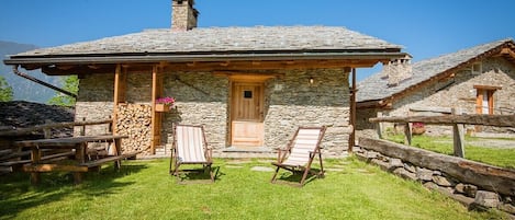 A stone cottage with a wooden door, two lounge chairs, and a stone wall.