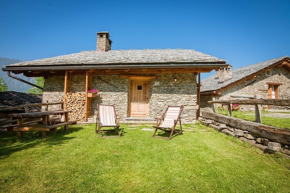 A stone cottage with a wooden door, two lounge chairs, and a stone wall.