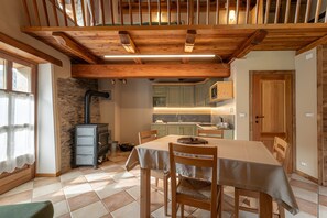 Zona pranzo con tavolo, sedie, camino e cucina sullo sfondo.