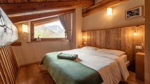 A wooden-paneled room with a bed, a window with a view of mountains, and a wall-mounted light fixture. - Chalet 'Civico 1 ' with Mountain View, Private Garden and Wi-Fi (Marmora)