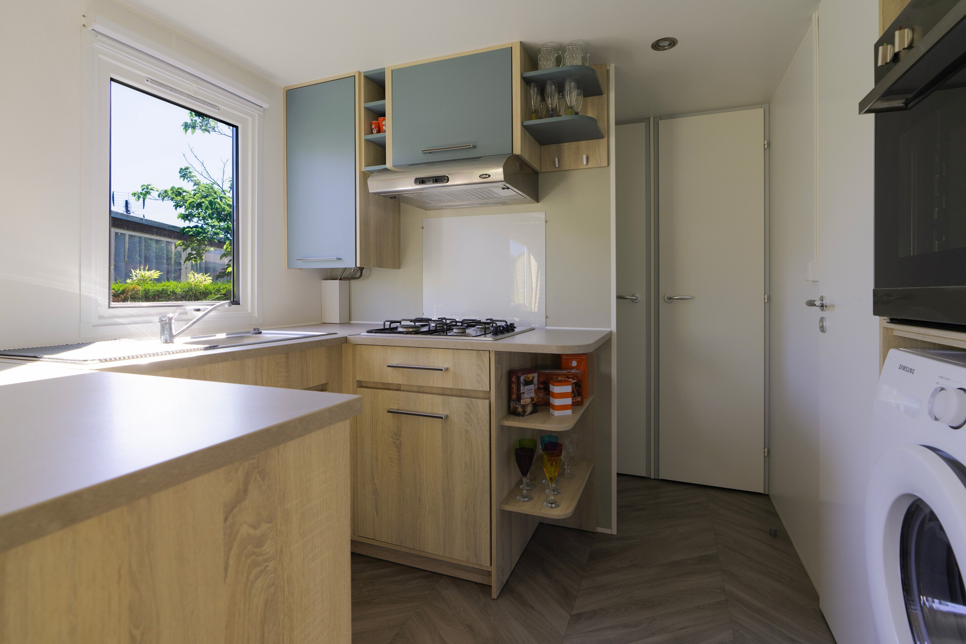 Une cuisine compacte avec des meubles en bois, une cuisinière encastrée, une fenêtre et un lave-linge.