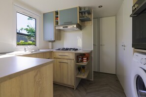 A compact kitchen with wooden cabinets, a built-in stove, a window, and a washing machine.