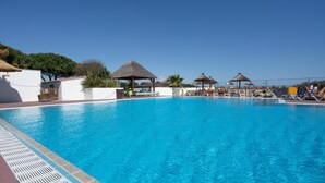 Une piscine entourée de murs blancs et d’arbres, avec des chaises longues et des parasols.