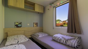Une chambre avec deux lits, une tête de lit en bois, une fenêtre avec des rideaux et une vue sur la verdure à l’extérieur.