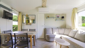 Un salon moderne comprenant un coin repas, un canapé, un téléviseur fixé au mur et une fenêtre avec des rideaux.