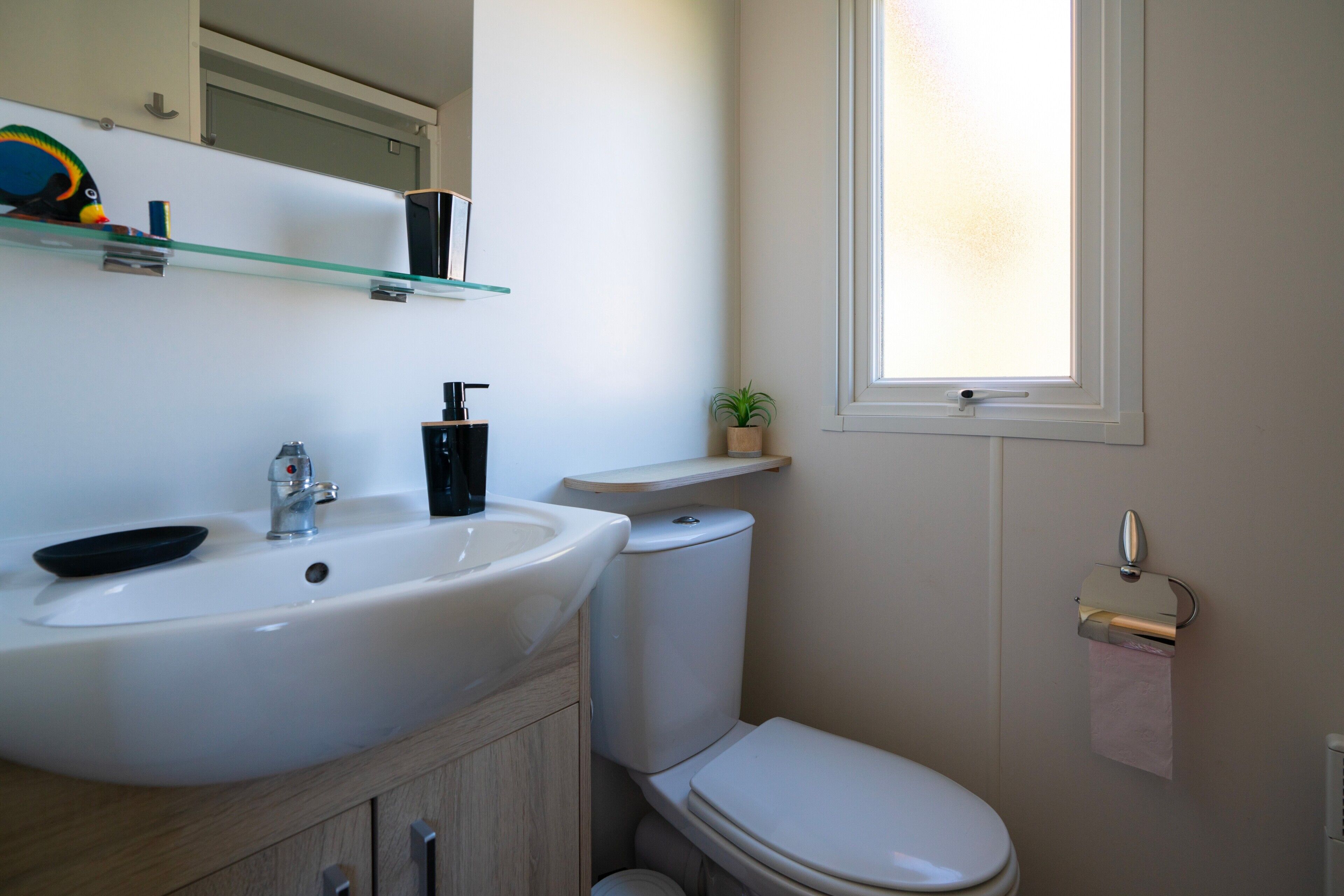 Une salle de bain avec un lavabo blanc, des toilettes et une fenêtre.