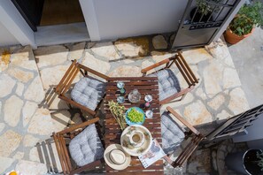 A stone patio with a wooden table, four chairs, a potted plant, and a small garden area.