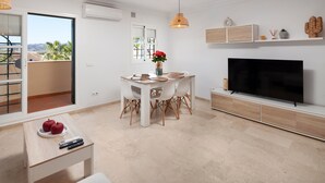 A modern living room with a dining area, a flat-screen TV, and a balcony with a view.