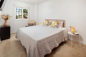 A bedroom with a large bed, a bedside table with a lamp, a chair, and a window with a view.
