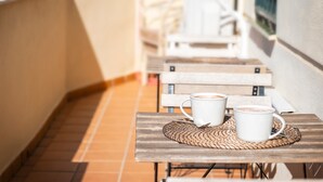 A narrow outdoor corridor with a tiled floor, a wooden bench, and a table with two white cups.