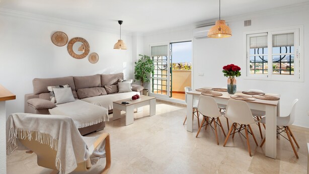 A modern living room with a sofa, coffee table, dining table with chairs, and a view through a sliding door.