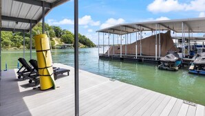 A covered dock area with a boat covered by a tarp, a yellow lifebuoy, and a row of jet skis. - Sleeps 26 lakefront w/ private dock & dance floor! (Lake Ozark)