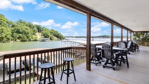 A covered deck with outdoor seating and a view of a lake and forest. - Sleeps 26 lakefront w/ private dock & dance floor! (Lake Ozark)