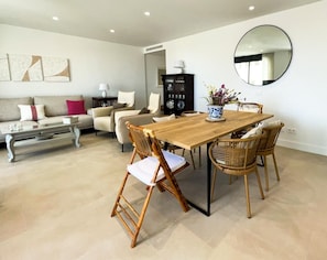 A dining area with a wooden table, wicker chairs, a vase with flowers, a round mirror, and a sofa with cushions. - Apartment 'Sun Garden' with Sea View, Wi-Fi & A/C (Torrox)
