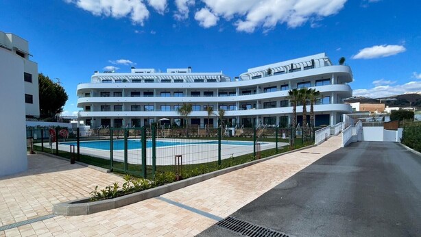 Un hôtel moderne à plusieurs étages, doté d’une piscine, de promenades pavées et surplombant un ciel d’un bleu éclatant.