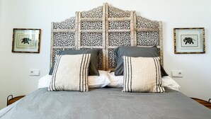 Un lit recouvert d’une couvre-lit grise, deux oreillers à motifs rayés et une tête de lit décorative ornée de sculptures complexes.