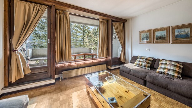 Una sala de estar con un sofá, una mesa de centro de vidrio y un banco junto a la ventana.