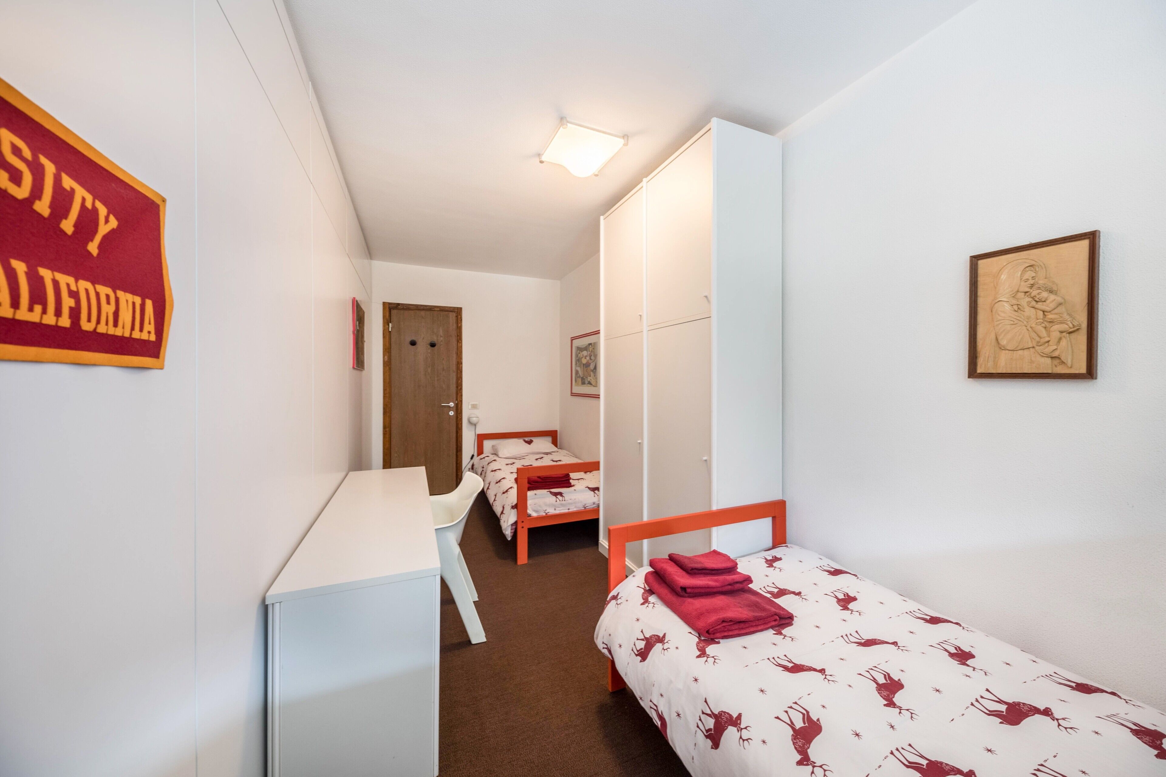 Habitación tipo dormitorio con escritorio, dos camas, una puerta y un letrero en la pared.