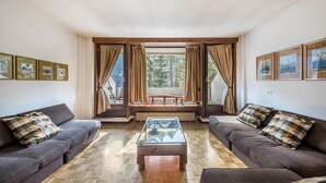 Una sala de estar con dos sofás, una mesa de centro de vidrio y vistas a través de ventanas grandes con cortinas.