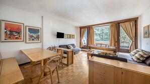 Una habitación con una mesa de comedor de madera, un sofá, un televisor y ventanas amplias con cortinas.