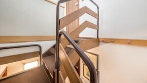 Una escalera de madera con barandales de metal, una puerta al fondo y un cuadro en la pared.
