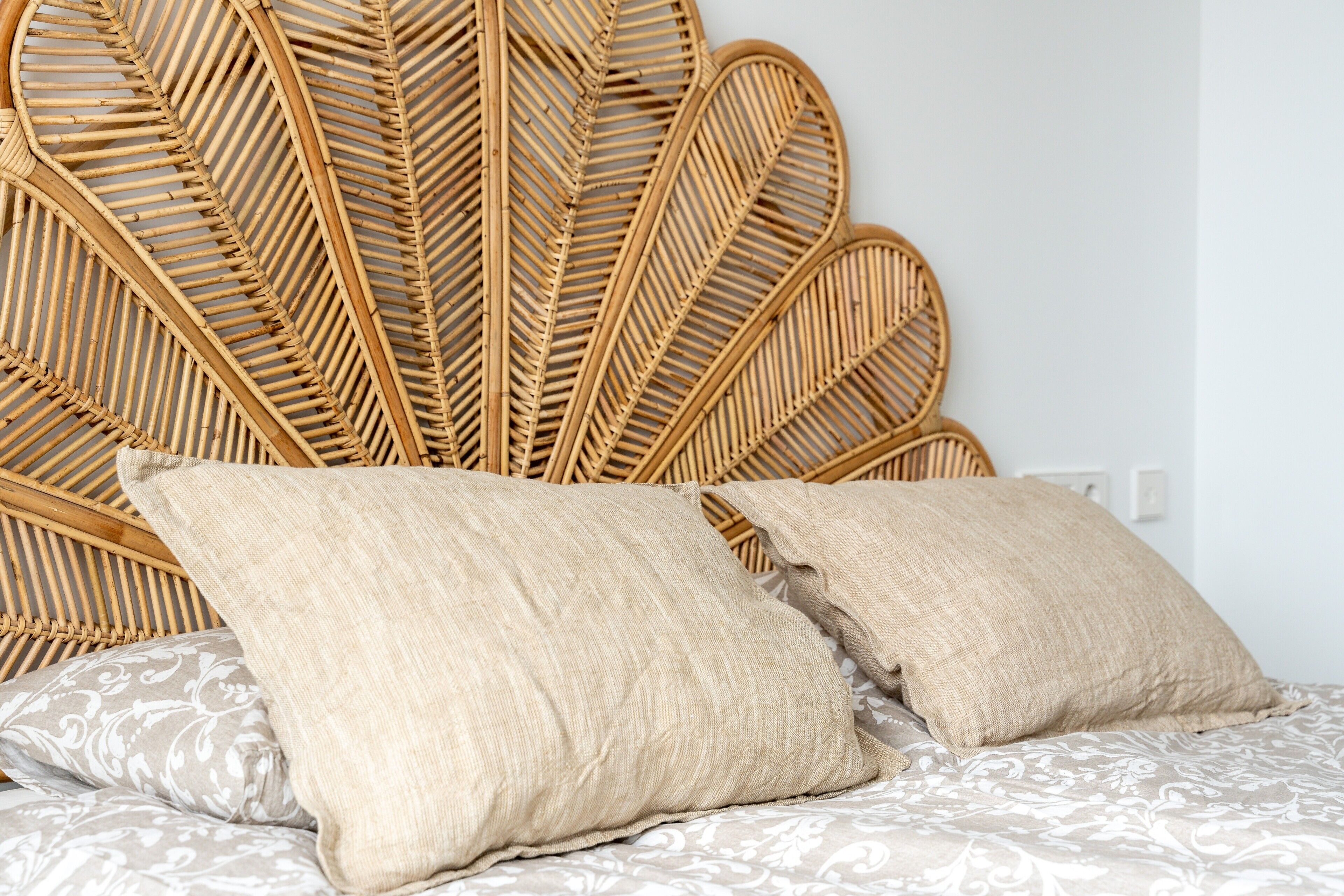 Una cama con cabecera trenzada, dos almohadas color beige y una colcha estampada.