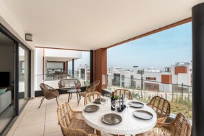 Een balkon met een ronde eettafel, rieten stoelen en uitzicht over de stad.