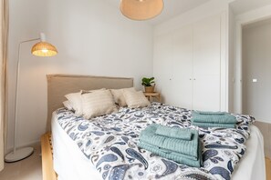 Een slaapkamer met een bed, kussens, een bedlampje, een plant en een kledingkast.