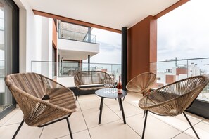 Een balkon met rieten stoelen, een klein tafeltje en een fles wijn.