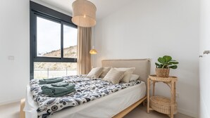 A modern bedroom with a bed, a bedside table with a plant, and a window with curtains. - Apartment 'Holiday Apartment Middle Views' with Sea View, Wi-Fi and Air Conditioning (FUENGIROLA)