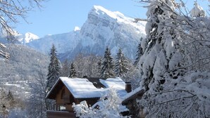 Un chalet en bois, dont le toit est recouvert de neige, entouré d’arbres chargés de neige et avec une montagne en toile de fond.