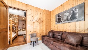 Un intérieur en bois avec un canapé en cuir marron, un fauteuil, un lit et un mur en bois orné d’une image d’ours.