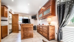 Une cuisine avec des meubles en bois, un îlot central, une télévision et une fenêtre avec des rideaux.