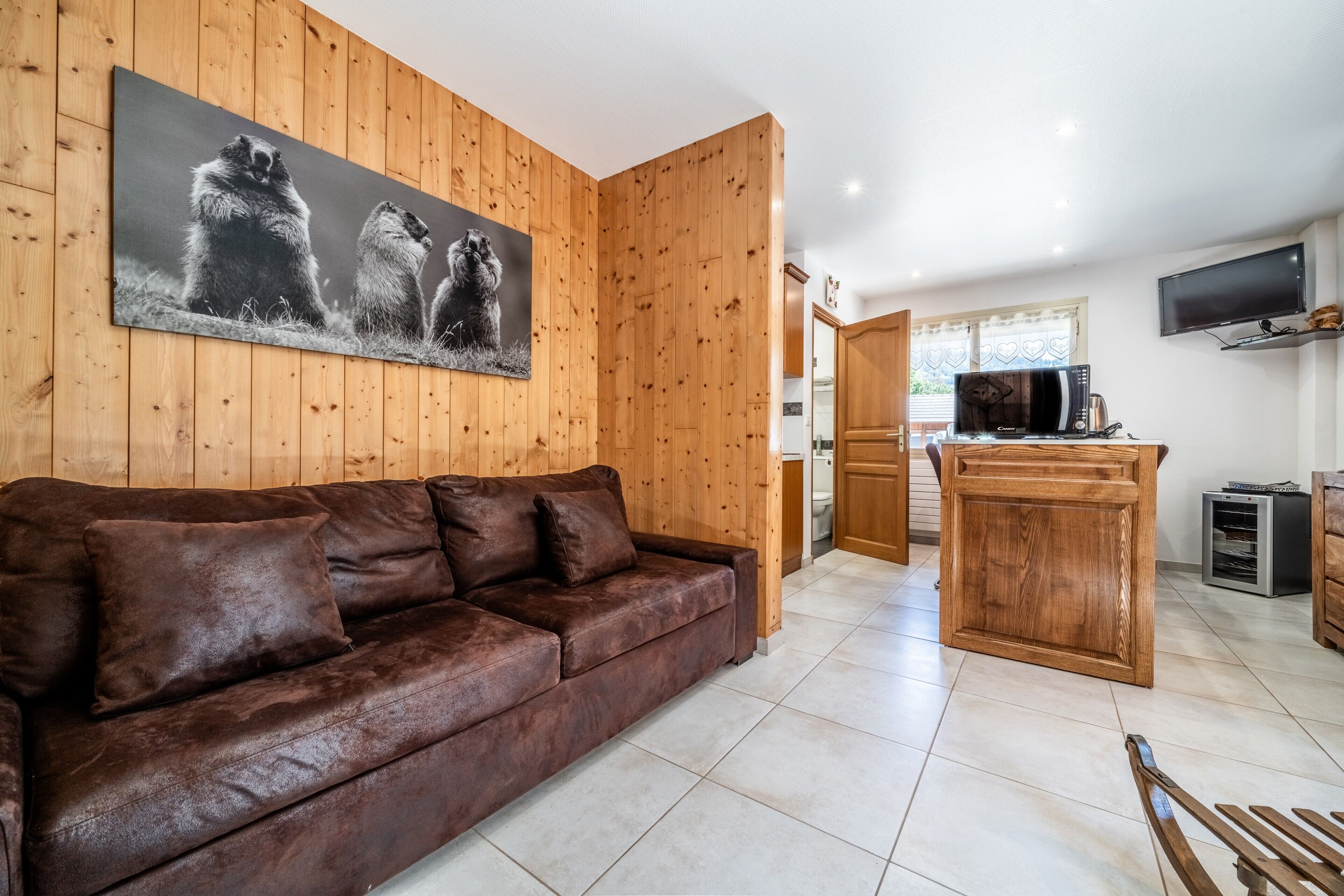 Ein Zimmer mit Holzvertäfelung, einer braunen Ledersofa, einer Küchenzeile und einem an der Wand befestigten Fernseher.